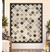 The completed Make It Scrappy Quilt, colored in elegant neutrals from the Botanical Sketchbook collection by White Owl Textiles, hung on a cream shiplap wall and staged with coordinating décor and furniture.