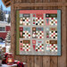 A digital mockup of the completed quilt, staged on a rustic wood wall with a red camper peeking into frame from the background.