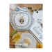 Finished cross stitch bee pattern laid on a wood table next to a bowl of applesauce.