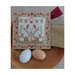 A photo of the finished pattern stitched onto a neutral finishing board on a wood table behind two eggs.
