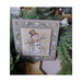 Photo of the cross stitch pattern with the finished pattern stitched onto a granite-gray finishing board in front of pine boughs.