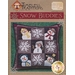 A decorative pillow cover titled Snow Buddies featuring a quilted design with nine patches, each containing snowmen and snowflakes in various colors. The background is dark plaid, and the design includes playful elements like hats and scarves on the snowmen. The top of the image has the Timeless Traditions logo and product title.