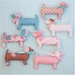 A collection of eight decorative fabric dogs in various colors and patterns, including pink, blue, and brown, arranged on a light blue background. Each dog features a different design, some with bows and patterns, showcasing a playful and whimsical style.