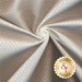 A close-up image of a white fabric with small white polka dots, displaying its smooth texture and sheen. A logo from Shabby Fabrics is visible in the corner.