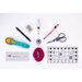 A flat lay arrangement of various sewing tools on a white background, including a rotary cutter, scissors, a pen, a marking tool, a spool of thread, pins in a holder, and two transparent rulers.