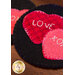 A close-up image of two decorative felt hearts in shades of red and pink, stitched onto a black background. One heart has the word LOVE and the other has XO embroidered on them.