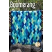 A colorful quilt titled Boomerang is displayed, featuring a diamond pattern with varying shades of blue and green. The quilt is hanging outdoors against a natural backdrop, and the logo for Jaybird Quilts is visible in the bottom right corner.