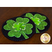 Two round coasters with a black background featuring a green shamrock design, placed on a wooden surface.