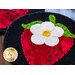 A close-up of a decorative wool coaster featuring a strawberry design, with a white flower and green leaves, set against a black background.