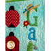 A colorful quilted wall hanging featuring two ladybug designs with polka dots, the word G a in decorative fabric letters, and decorative elements like a flower and a wide-brimmed hat.