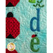 A close-up of a colorful quilt featuring the letters d and e, embellished with a green plant and a small ladybug, alongside red and black ladybug designs on a light blue background.