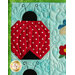 A quilted fabric design featuring a large red ladybug with white polka dots, against a light blue background. The ladybug has a black head and antennae, and is surrounded by floral patterns stitched in various colors.