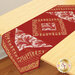 A decorative table runner featuring a rich red and cream design with geometric patterns and paisley elements, laid across a wooden table.