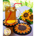 A mason jar filled with iced tea and a lemon slice, accompanied by a red straw and placed on a sunflower-shaped coaster. Next to the jar, there are artificial sunflowers, adding a bright, colorful touch to the scene. Underneath the jar are two wool Mug Rug coasters made to look like sunflowers.