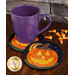 A purple mug is placed on two Halloween-themed coasters featuring pumpkins, surrounded by candy corn on a wooden surface.