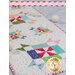 A colorful quilted table runner featuring a pattern of star blocks in various shades of red, green, blue, and pink, accented with white fabric dotted with colorful specks. There are felted white balls placed along the runner, and a logo for Shabby Fabrics in the right corner.