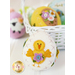 A decorative white Easter egg with a yellow chick and a purple flower sewn on it, surrounded by colorful eggs in a white basket.