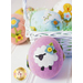 A basket filled with decorative felt eggs in various pastel colors, featuring a purple egg adorned with a sheep design and small flower embellishments. Other eggs in the background include a blue one with a bunny and a yellow one with a chick.