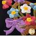 A close-up of a wool floral arrangement featuring colorful flowers in a basket, with a purple bow at the base, set against a dark background.