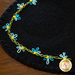 A close-up of a black felt fabric with yellow, blue, and white embroidered flowers along the edge, showcasing a decorative stitch pattern.