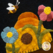 A colorful felt design featuring a buzzing bee, bright flowers in blue, pink, and yellow, and a textured sunflower in orange and brown, all set against a black background.