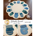 A circular wool mat featuring decorative mittens in shades of blue and green arranged around the edge. The center has a light cream color with snowflake designs. The design is titled Simply Sweet Wool Mat and labeled for January.