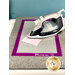 An iron sits on a gray mat with a pink fabric square and a purple border, labeled Appli-Fuse Mat.