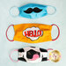 Three colorful cloth masks displayed in a vertical stack. The top mask is blue with a black mustache design, the middle mask is bright yellow with the word HELLO! in a comic-style speech bubble, and the bottom mask features a cow pattern with a pink and black design. A logo for Shabby Fabrics is visible in the bottom right corner.