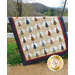 A patchwork quilt with a diamond pattern featuring colorful ties hangs on a fence in a natural landscape.