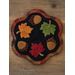 A black wool candle mat with maple leaves and acorns on a wood desk