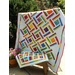 A colorful quilt with a geometric pattern of multicolored squares is displayed beside a matching mini quilt.