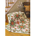 A quilt draped over a wooden chest in a cozy room. The quilt features vibrant floral patterns in red, pink, and green, with intricate detailing. In the background, a staircase and a chair with a decorative pillow can be seen.**Concise alt text (100 characters):** Floral quilt draped over a chest, featuring red and green patterns in a cozy room setting.