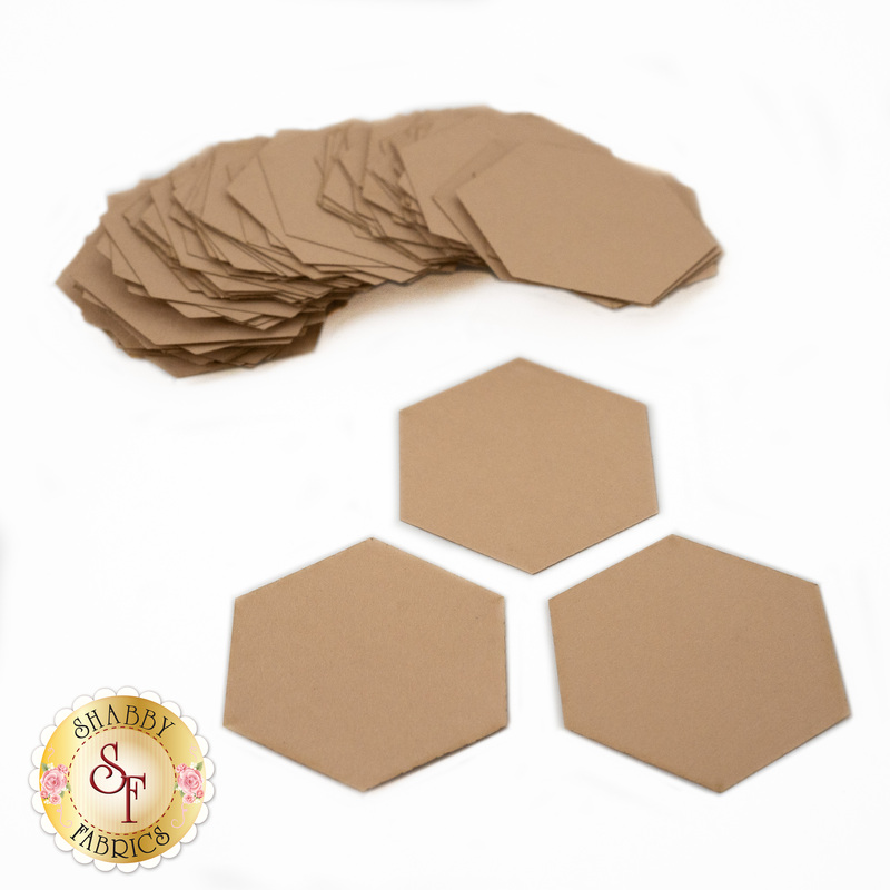 A stack of brown hexagonal fabric templates is arranged with three hexagons placed in front. The background is white, and a logo for Shabby Fabrics is visible in the corner.