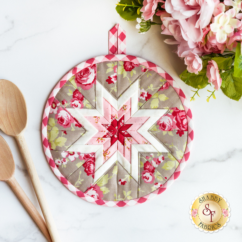 Grey and red floral folded star hot pad on a white marble countertop with wooden spoons and pink flowers