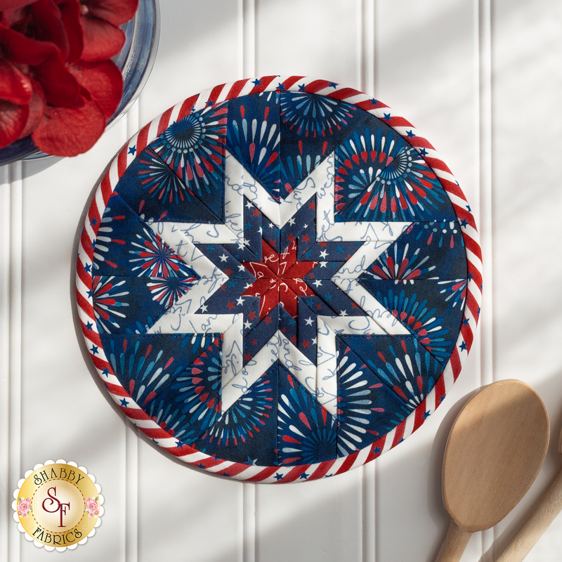 Round navy blue hot pad featuring a central star and firework motifs with red and white border.