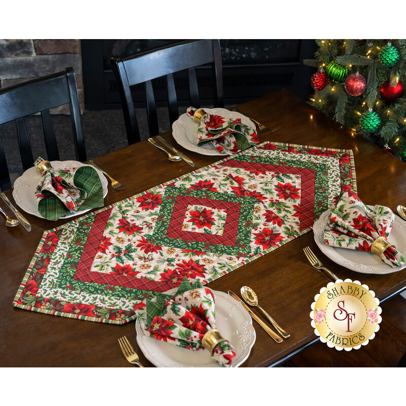 Christmas themed floral table topper on wood table next to matching cloth napkins. 