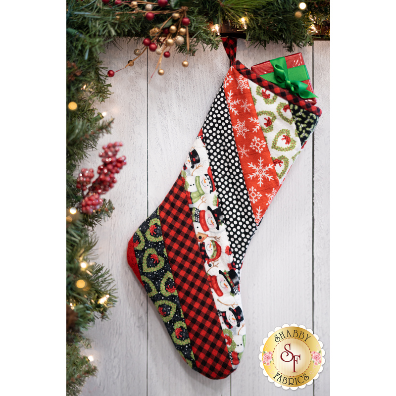 Hanging holiday stocking made from strips of Christmas themed fabric in red, black, and white.