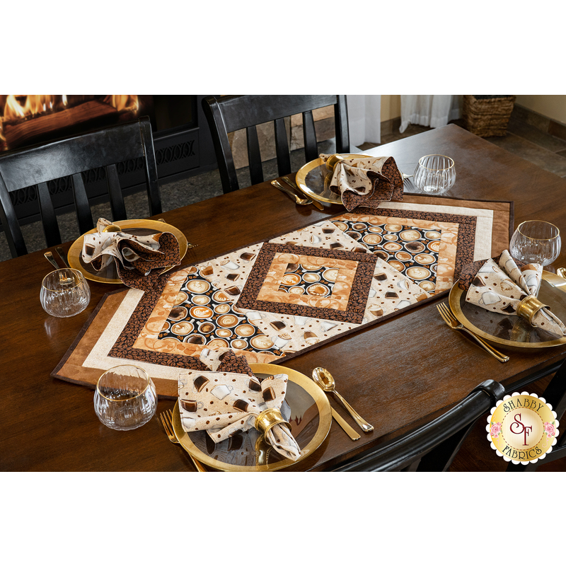 Table runner with central diamond design and angled strips the ends made of coffee themed fabrics in neutral colors.