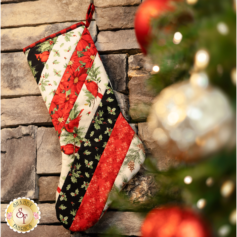 Hanging holiday stocking made from strips of Christmas themed fabric in red, black, and white.