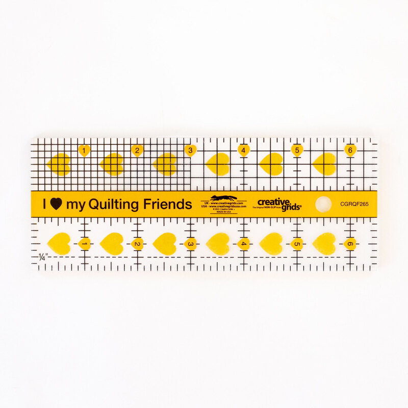 A clear acrylic quilting ruler with yellow hearts and geometric shapes, labeled with measurements in inches.