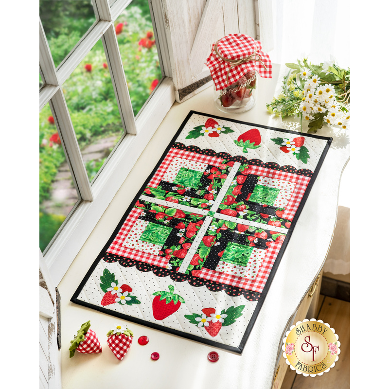 Table runner made of strawberry themed fabrics and featuring strawberry shaped appliqué on the ends.