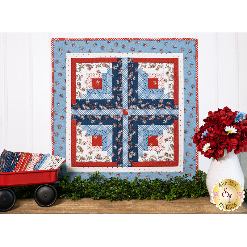 Wall hanging made of strips of red white and blue fabric featuring florals, paisleys, and gingham prints.