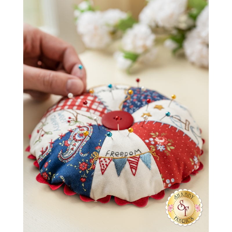 Round pin cushion made from triangle pieces of fabric with patriotic embroidery and a button middle.