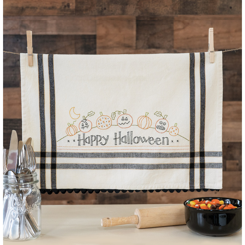 A kitchen towel embroidered with Happy Halloween and pumpkins hanging from clothes pins