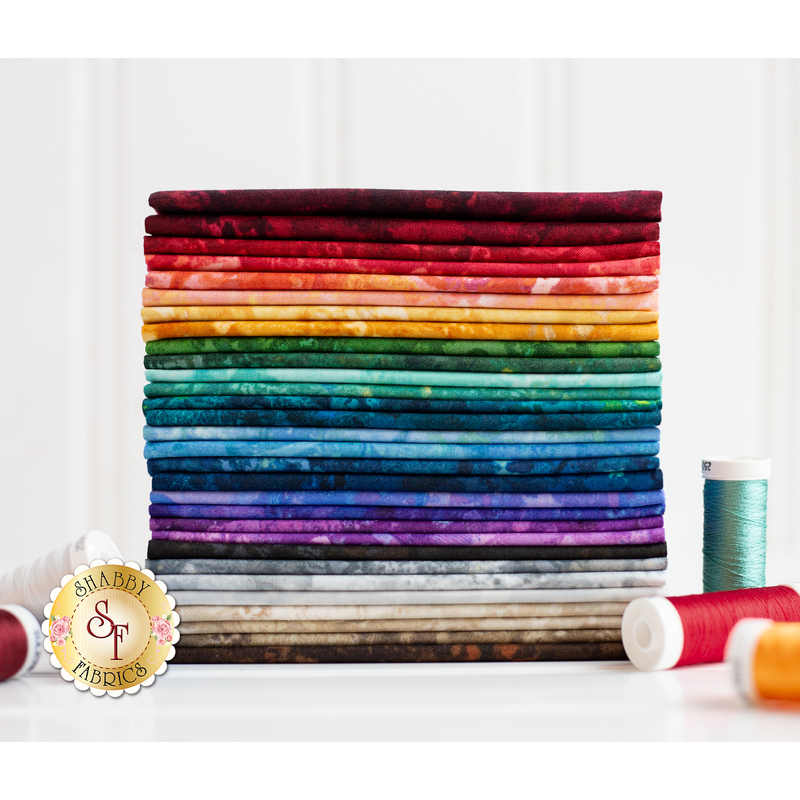 A stack of red, orange, yellow, green, blue, purple, and tan fabrics against a shiplap background