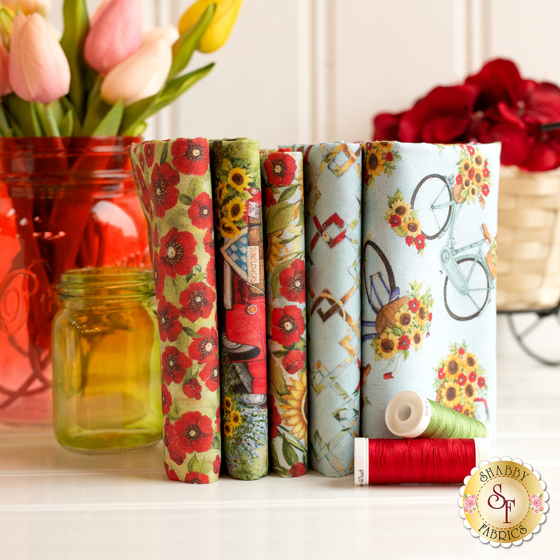 A collection of folded fabric swatches in various floral and patterned designs, positioned next to a spool of red thread and a mason jar filled with tulips.