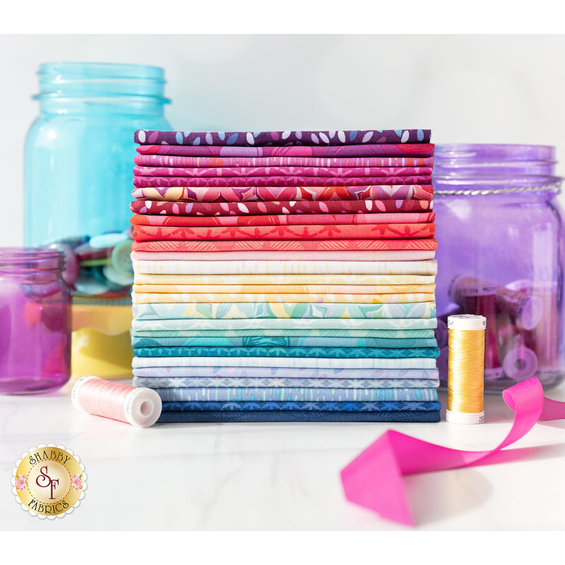 A stack of colorful fabric bolts arranged in a gradient pattern, with jars of buttons and spools of thread in the background. The fabrics feature various designs and colors, ranging from vibrant reds and purples to soft blues and whites.