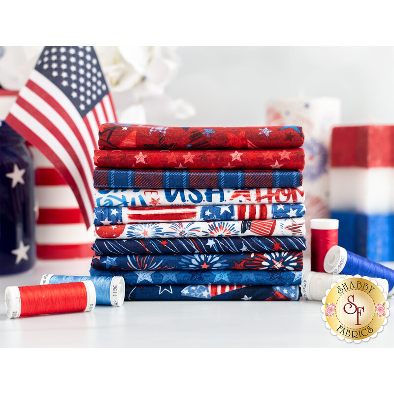 A stack of colorful fabrics in red, white, and blue, featuring patriotic patterns such as stars and stripes. Spools of red and white thread are placed nearby, and American flags are visible in the background.