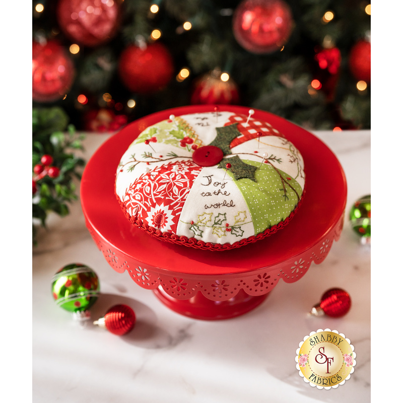 Red, green, and white, pincushion made of Christmas themed fabrics, accented with red button and holly leaf appliqué