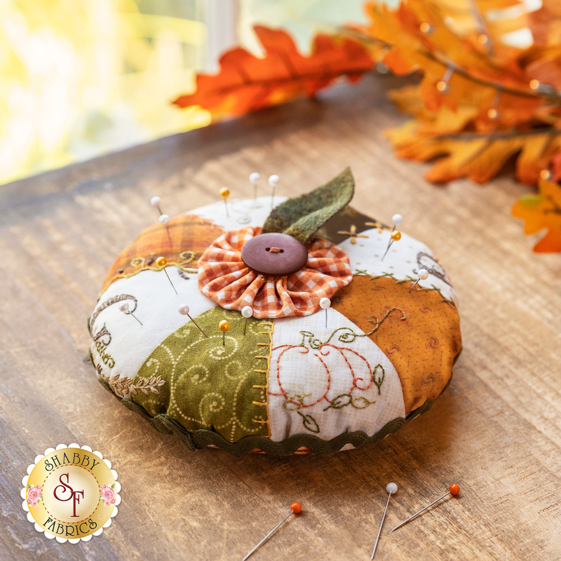 An orange, white, and green pin cushion with a small button topper on a wood table